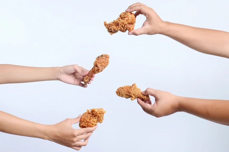 Hands sharing pieces of golden fried chicken