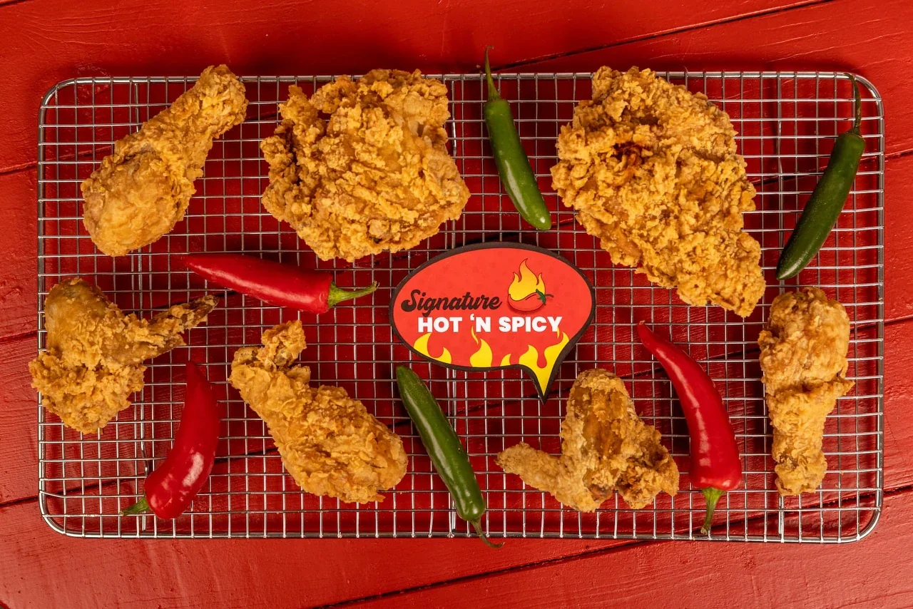 Signature Hot 'N Spicy fried chicken on a rack with fresh chillies